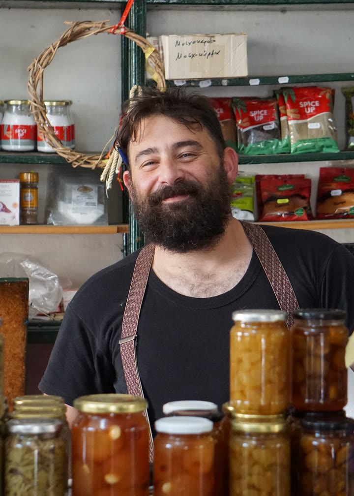 A shop owner smiling behind jars of preserves