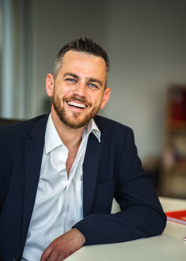 A business owner in a navy jacket smiling in his office